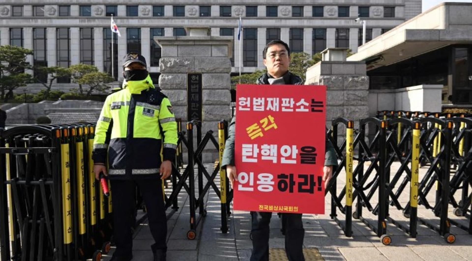 宪法法院16日上午就尹锡悦弹劾案举行首次会议。一名在外面抗议的男子举牌写著“宪法法院必须立即接受弹劾动议！”。