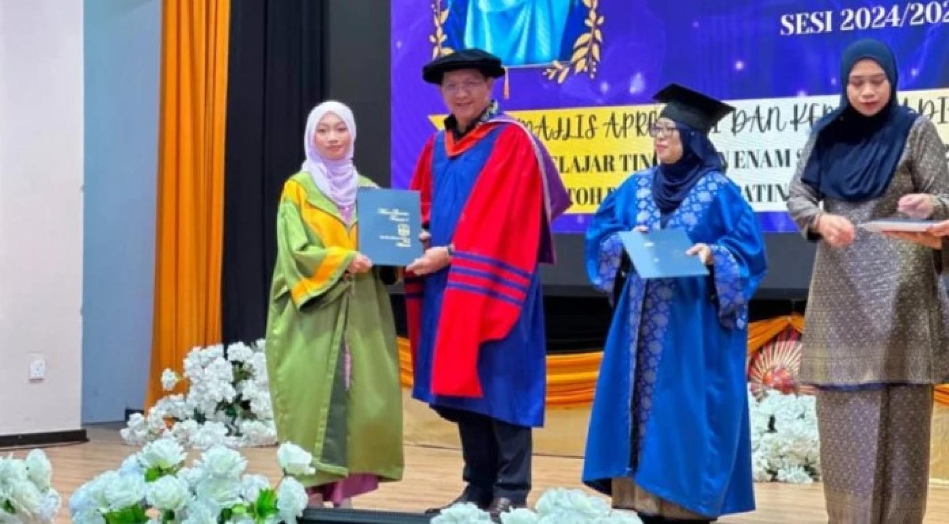 沙菲阿末医生（Dr Safiee Ahmad）在达罗民众会堂举行的“2025年达罗杜潘拿督巴丁宜哈查诺玛国中学生表扬与成果嘉奖典礼”上，颁发嘉奖证书予其中一名受表扬学生。