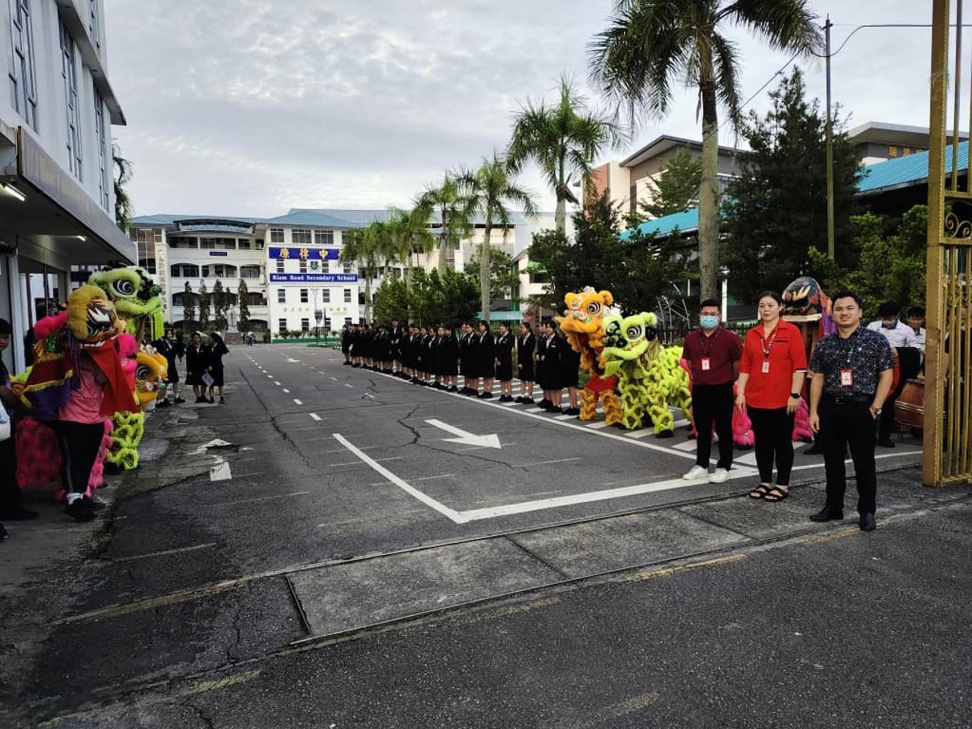 廉律中学校长江佩娟与联课副校长康亚雄清早站在校门迎接返校学生，以亲切问候与热情行动，展现校方向学生无微不至的关怀与支持。