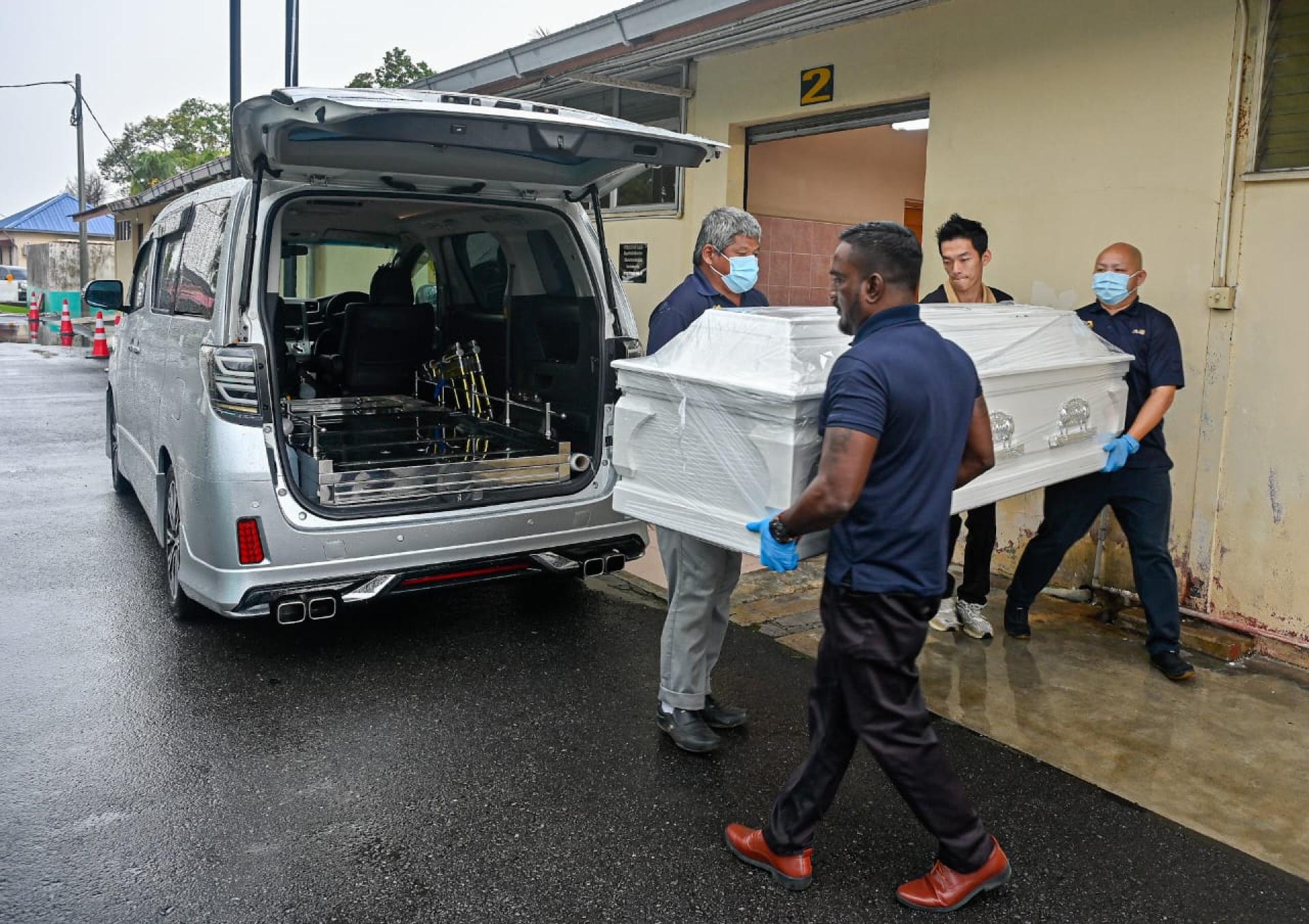 殡葬业者把死者灵柩抬上车。