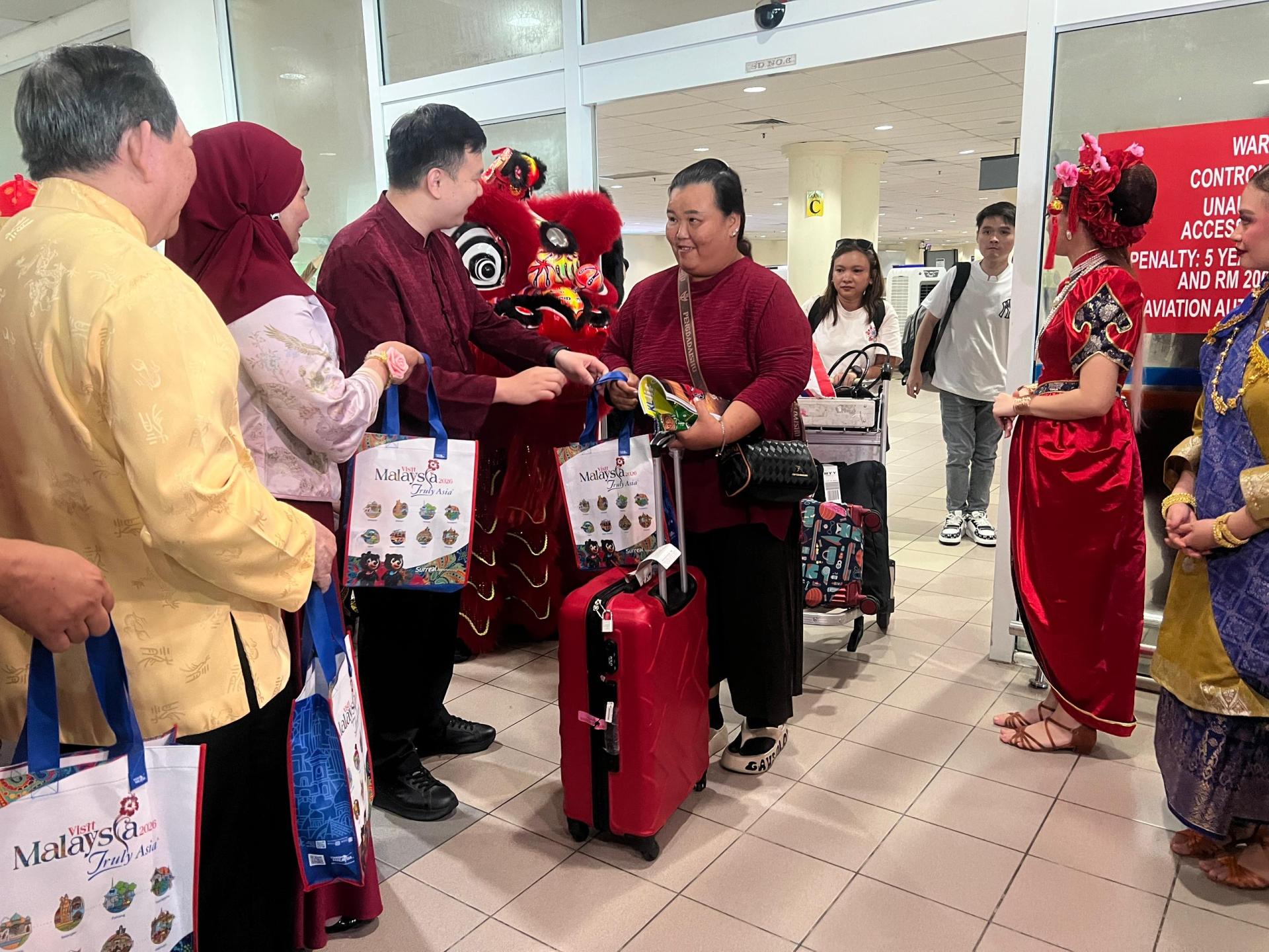 旅游、艺术及文化部副部长赵俊文（左3）派年柑与访马2026纪念品予抵达访客，现场气氛喜庆。