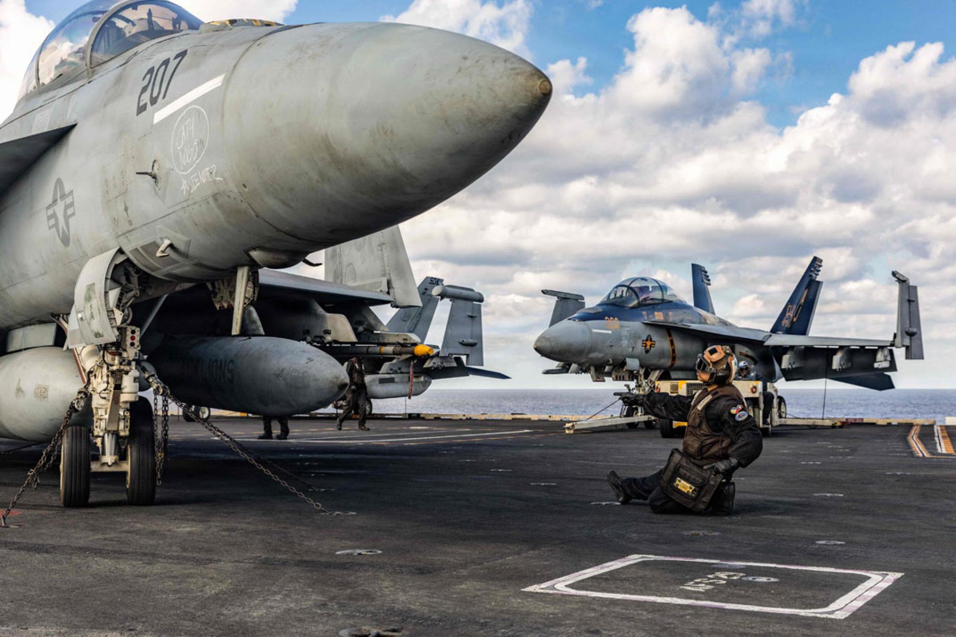 一名美军向“福特”号航空母舰上的F/A-18F超级大黄蜂战斗机发出信号。“福特”号航空母舰正支援对伊朗的军事行动。