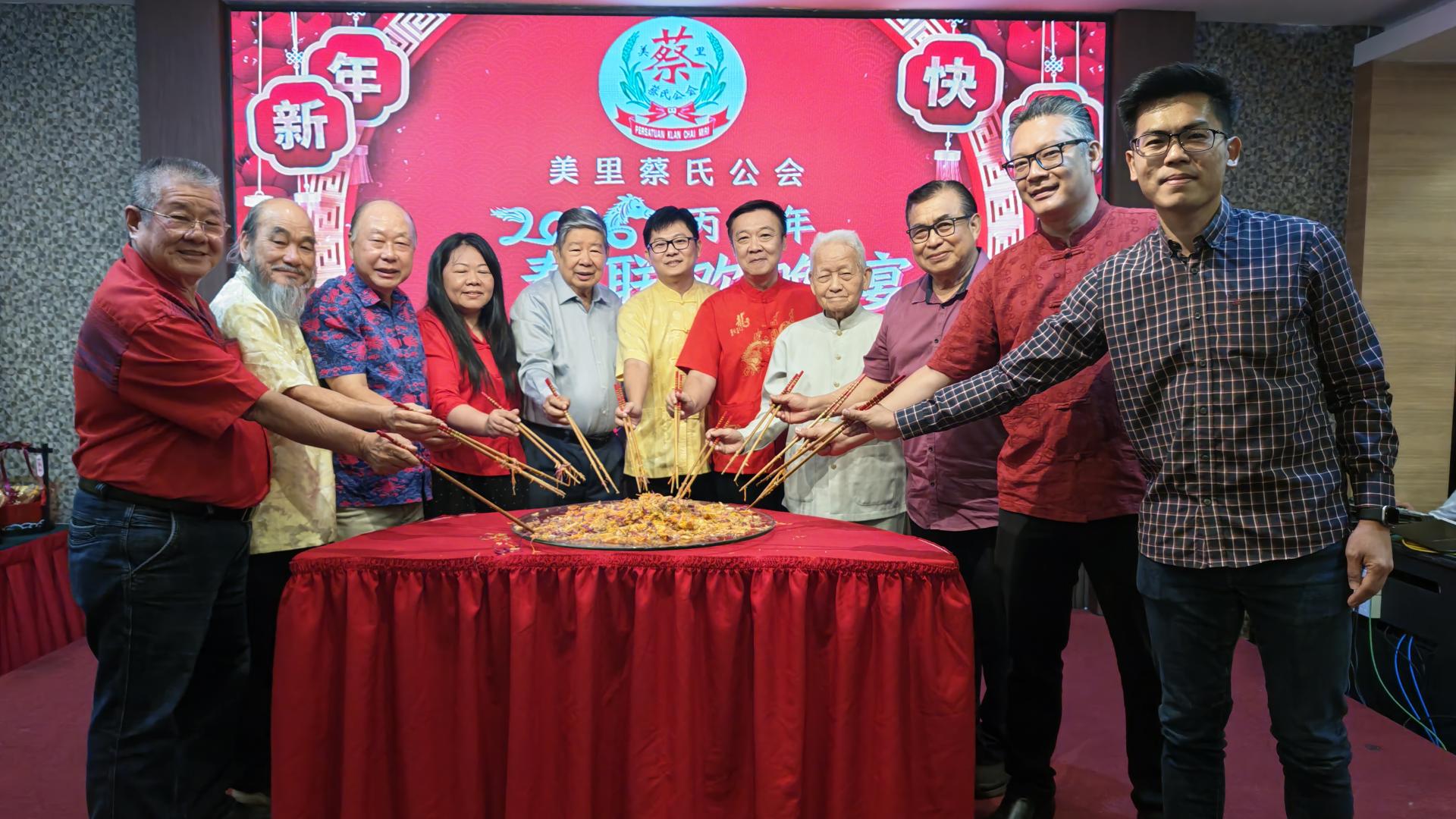 b. 主宾桌嘉宾与理事们在晚宴上联合捞生。左起为蔡氏公会财政蔡顺安、永久名誉主席兼会务顾问蔡明耕、永久名誉顾问兼署理主席蔡明健、砂旅游部副部长兼卑尔骚区议员拿督陈超耀的代表蔡玮意市议员、永久名誉会长蔡增城、筹备会主席蔡明勇、主席蔡明敏、永久名誉会长蔡高船、永久名誉顾问本固鲁蔡刚明、美里市长兼埔奕区议员俞小珊的代表余忠明市议员，以及马来西亚旅游、艺术及文化部副部长兼美里区国会议员赵俊文的代表罗立原律师。