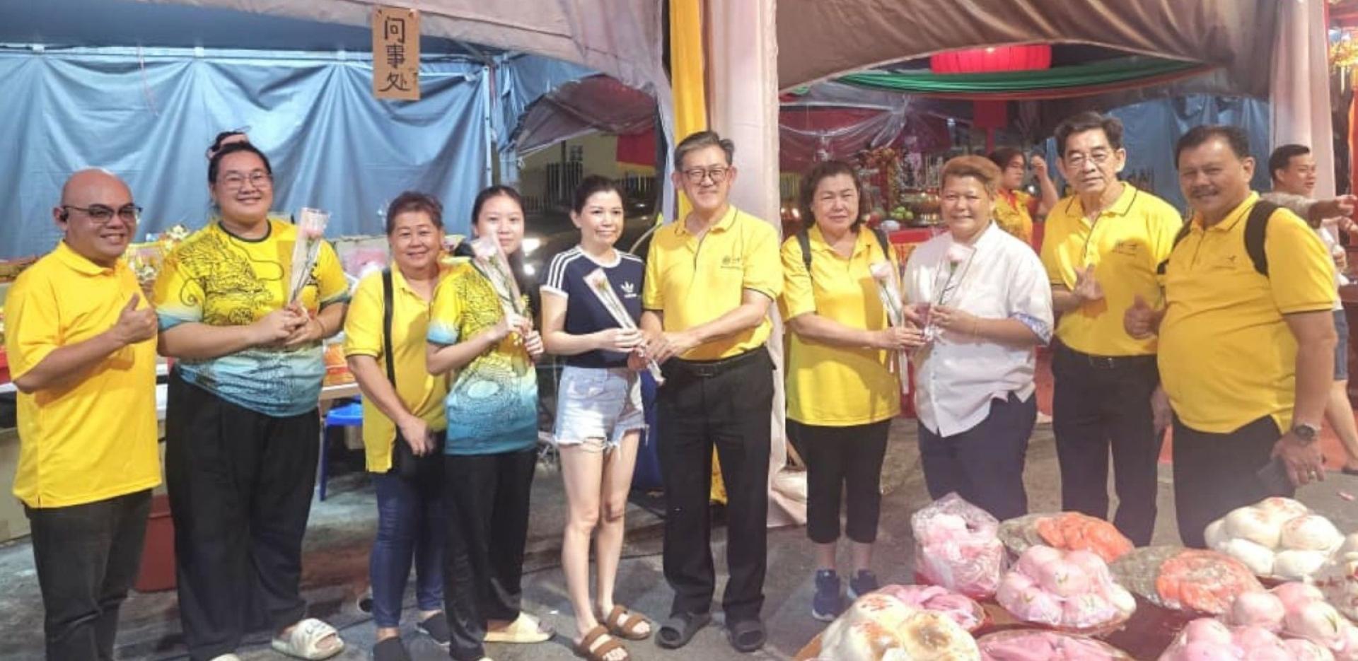 砂人联党峇都林当支部东哥团队于昨晚（8日），在达万都顺科丹地路的石皇仙祖千秋宝诞庆典帐篷处设流动柜台服务，贴近民众服务并应景庆祝38国际妇女节，由该支部主席薛华东（左6起）、妇女组主席甲必丹何月明在现场赠送康乃馨鲜花予女士。