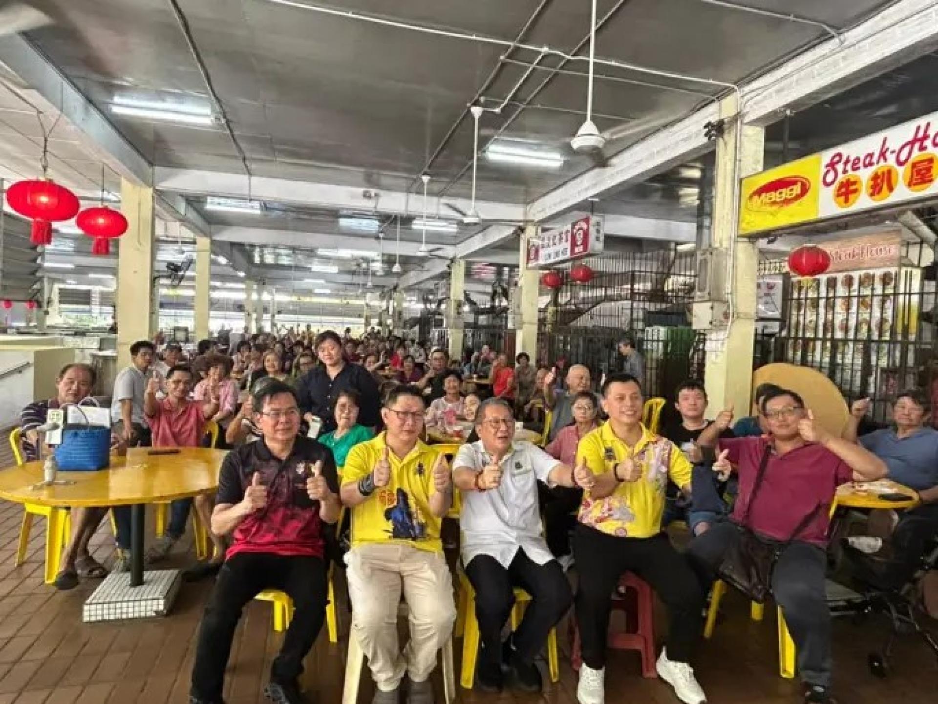 黄鸿圣（前排白衣）于2026年5月5日在毕达拿市场与小贩交流。