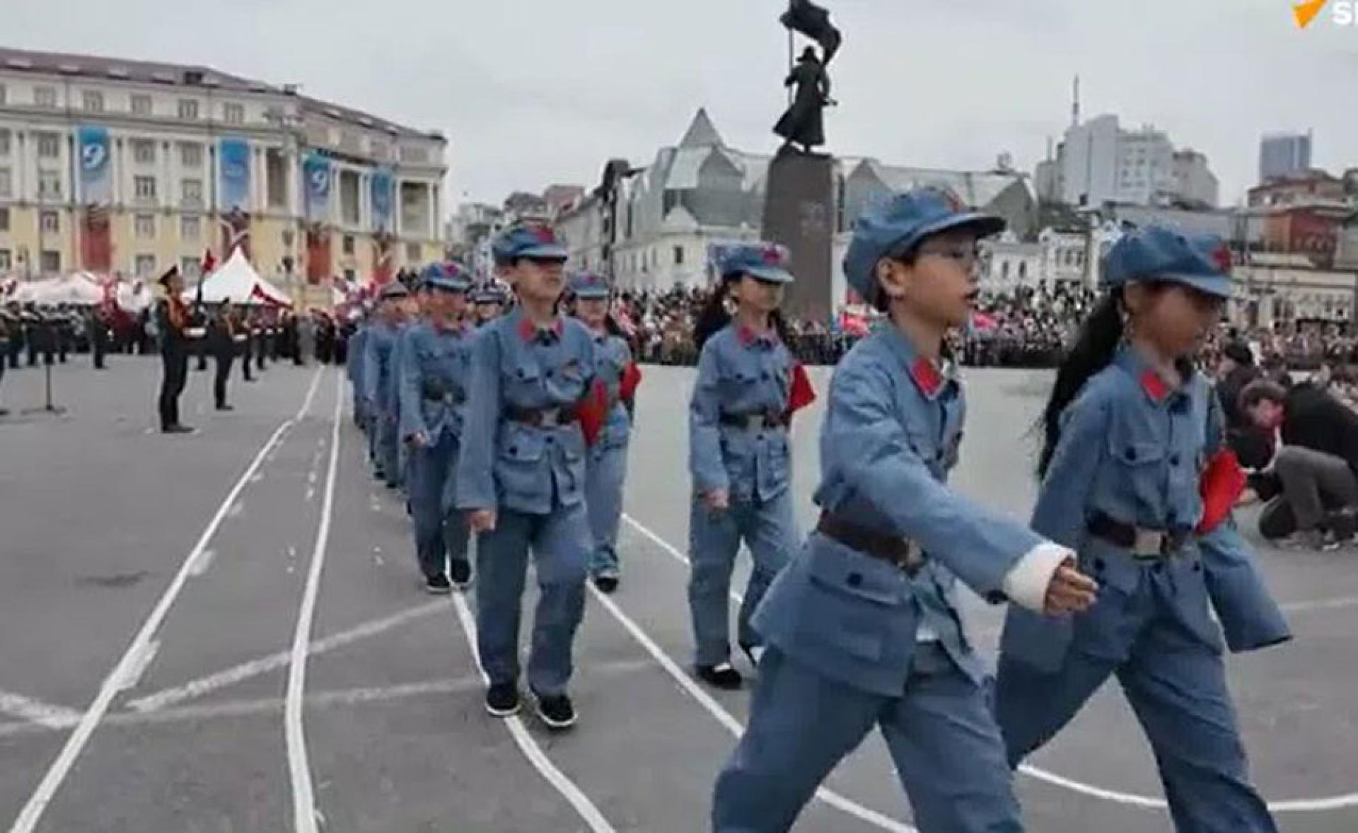 中国小学生身穿仿八路军军服，排成两列从广场走过。