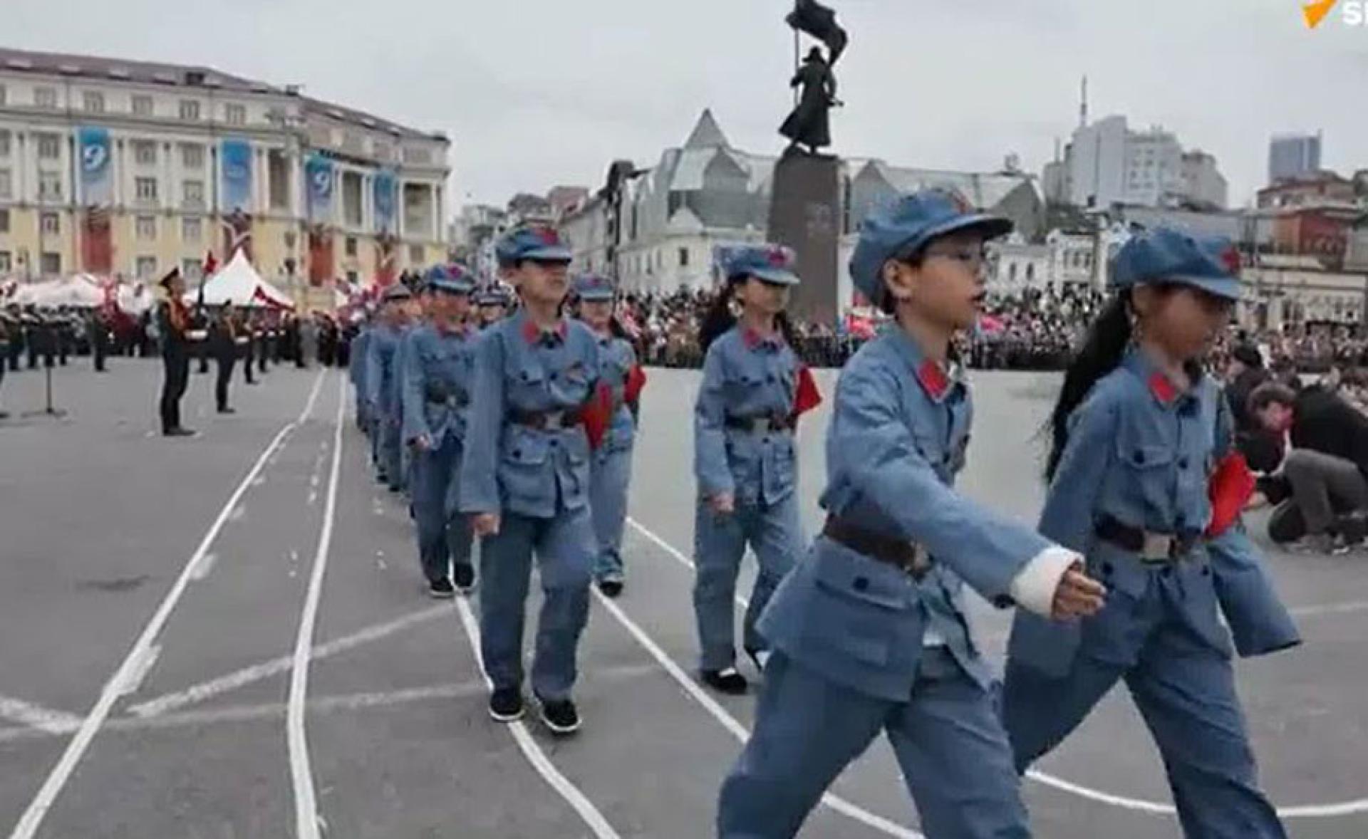 中国小学生身穿仿八路军军服，排成两列从广场走过。