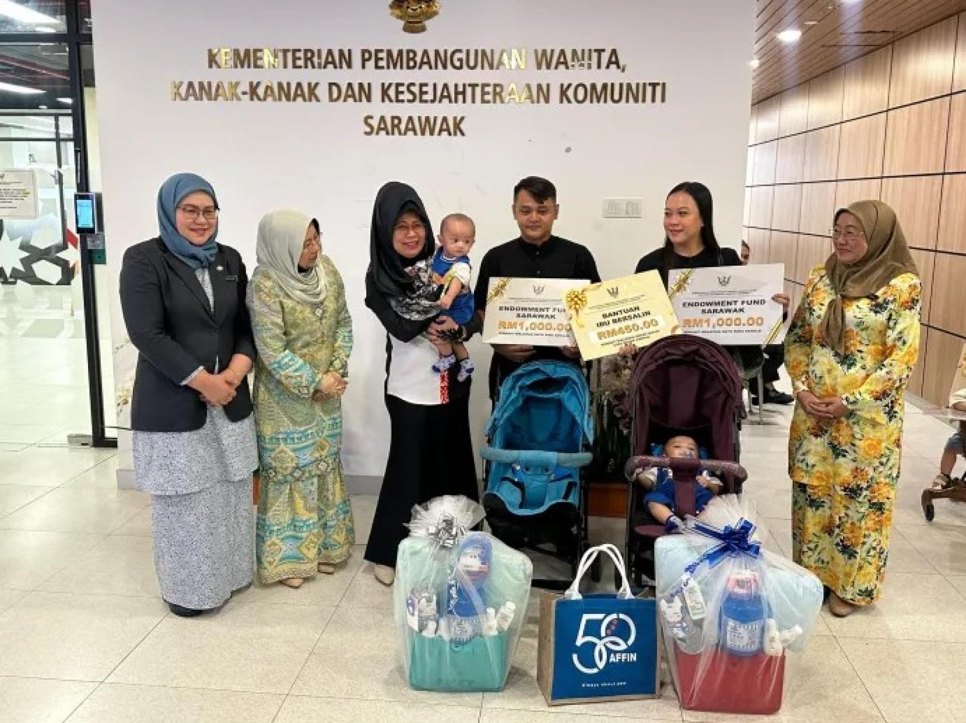 拿督斯里陈赛明（左3）于2026年6月8日在古晋Baitul Makmur 2大厦举行的教育储蓄基金颁发仪式上抱着一名婴儿，与出席者互动。