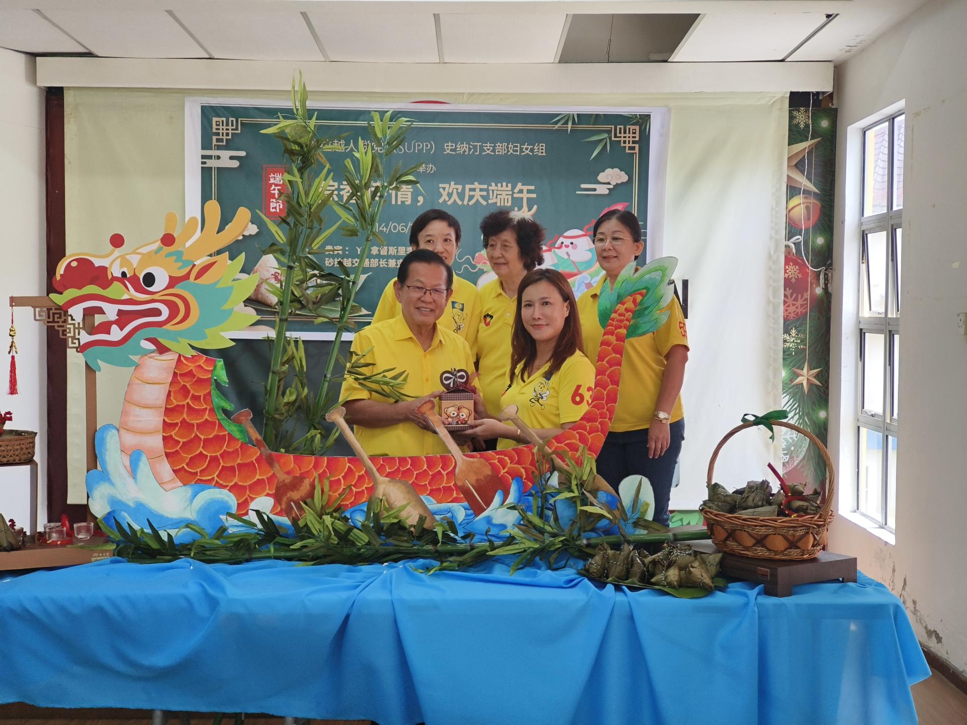 联合筹备会主席邬媚芬（前右）赠送纪念品予拿督斯里李景胜（前左）后，与妇女组主任兼市议员田秀兰（后右）、联合筹备会主席赖桂花（后中）及联合筹备会主席罗佩螢（后左）在端午节主题龙舟布景前合影留念。