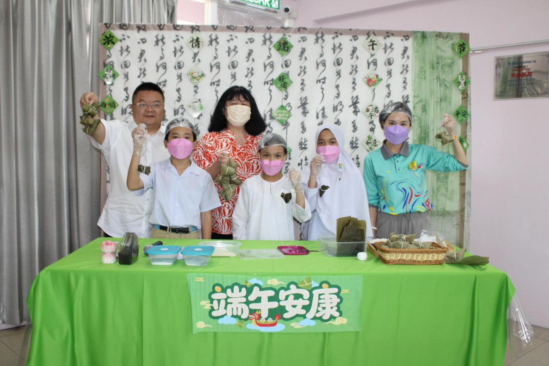 左二陶美华校长与胡婷老师（右一）及学生们展示粽子成品