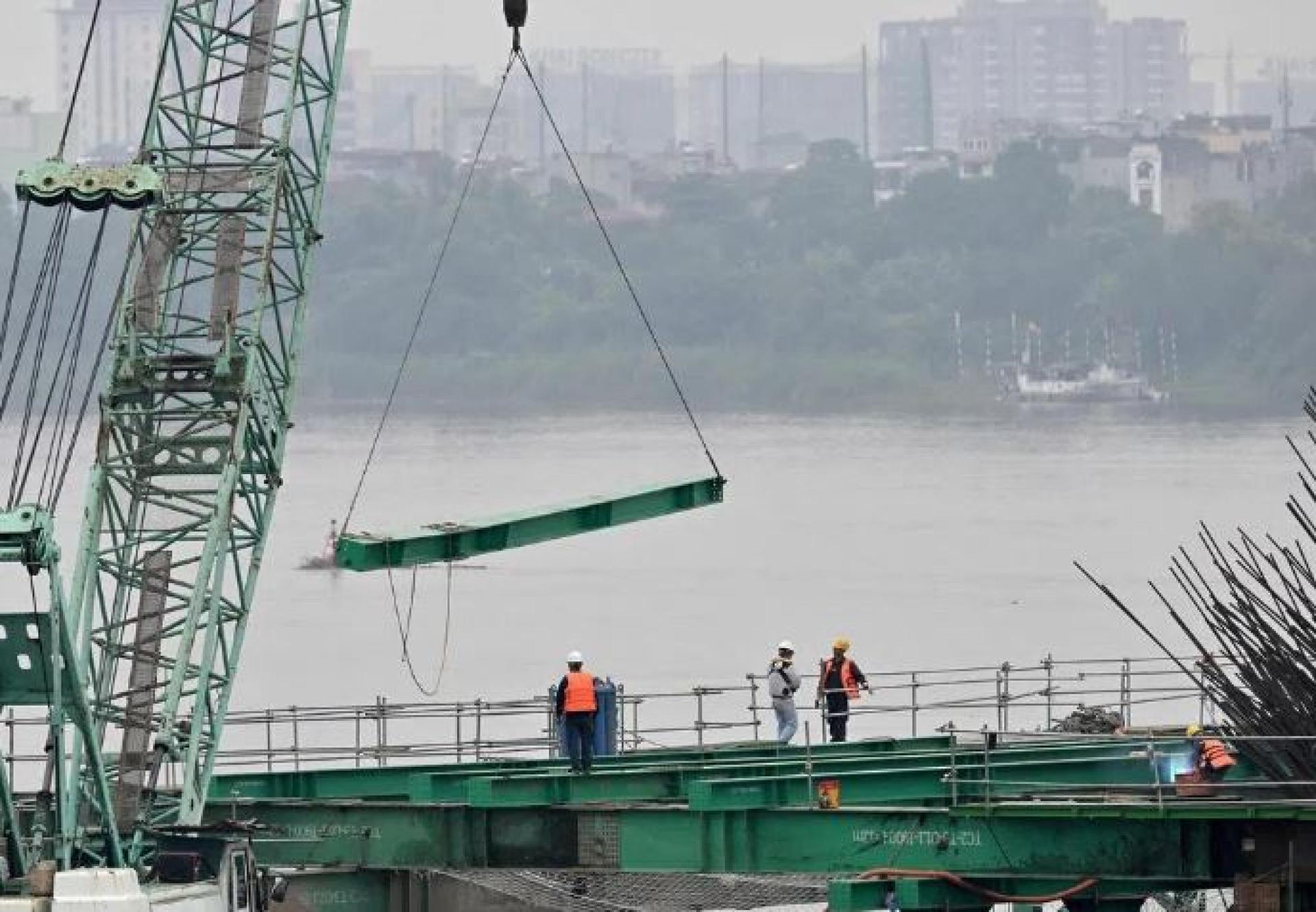 6月16日，工人们在越南河内使用重型建筑设备建造一座横跨红河的桥。