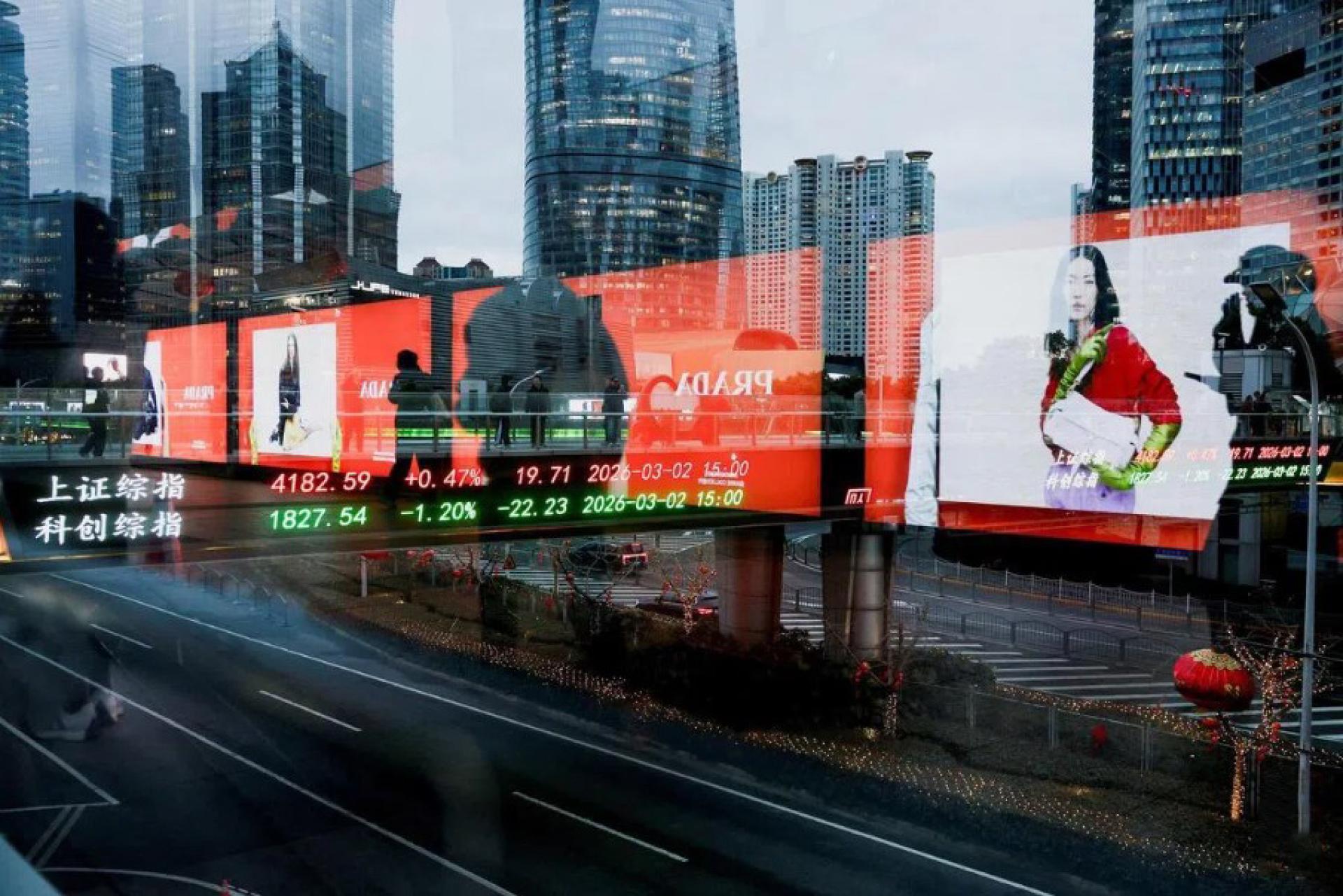 图为2026年3月2日，行人在中国上海陆家嘴金融区的人行天桥上穿行，背景的电子显示屏正展示上海股市指数。 （档案照片）