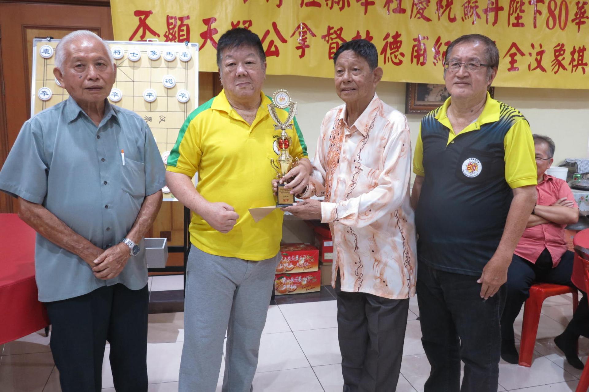 汶莱象棋公会名誉顾问拿督斯里沈炜翔颁发冠军奖杯予棋王周荣安。左一为该会主席陈仙福