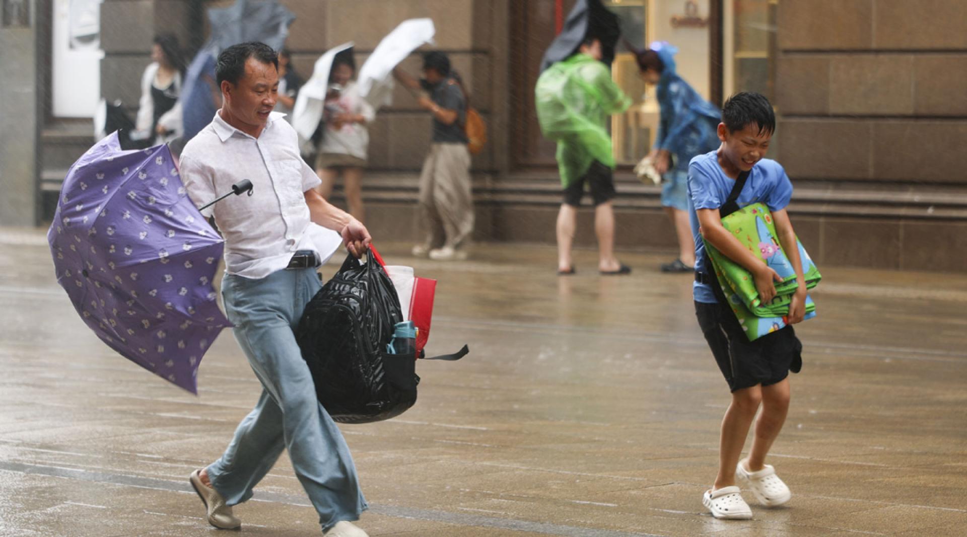 8月9日，在上海黄浦区南京东路上，一位父亲陪同孩子冒雨前行。