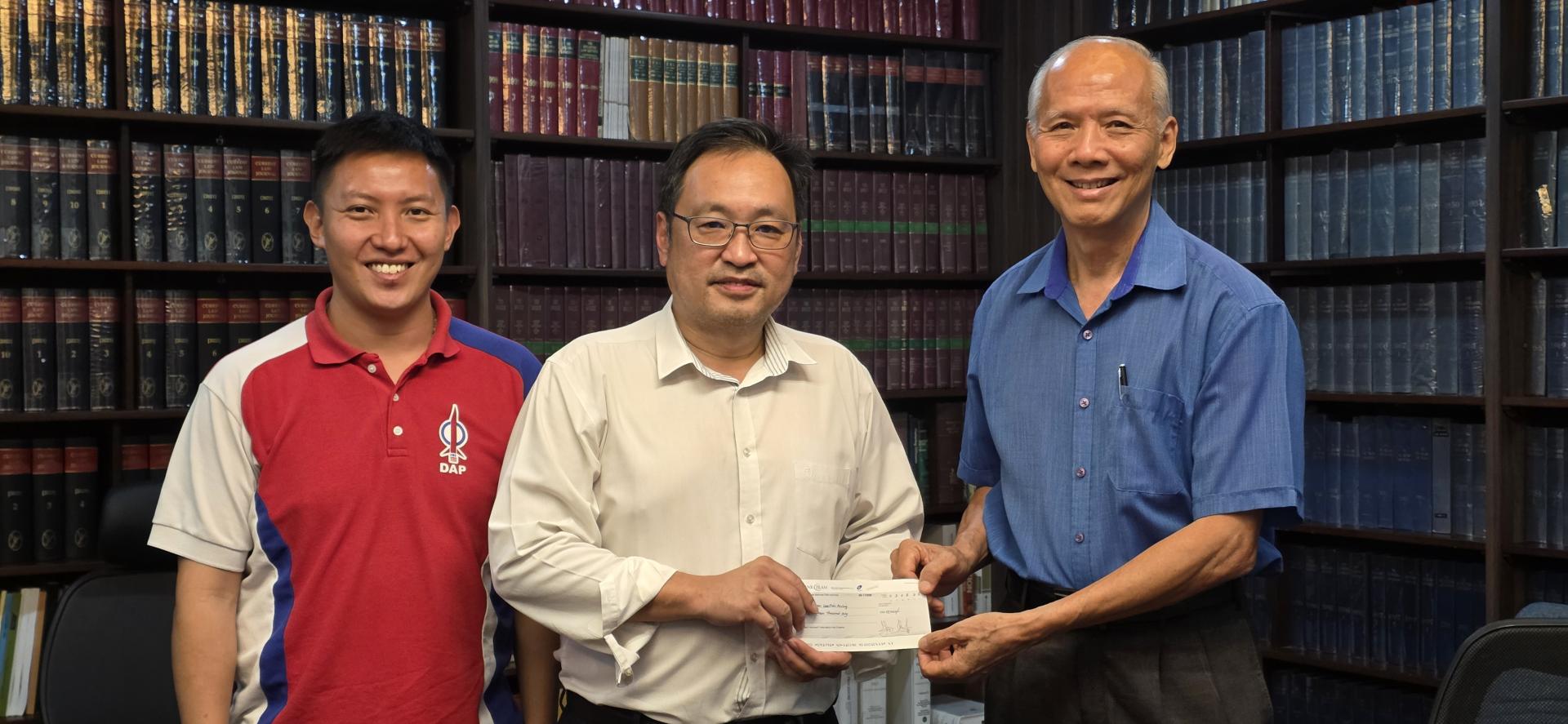 实旦宾区国会议员张健仁（中）在其特别助理沈杰龙（左）的陪同下，即席移交拨款支票予古晋拉萨利安基金会执行秘书陈春荣（右）。