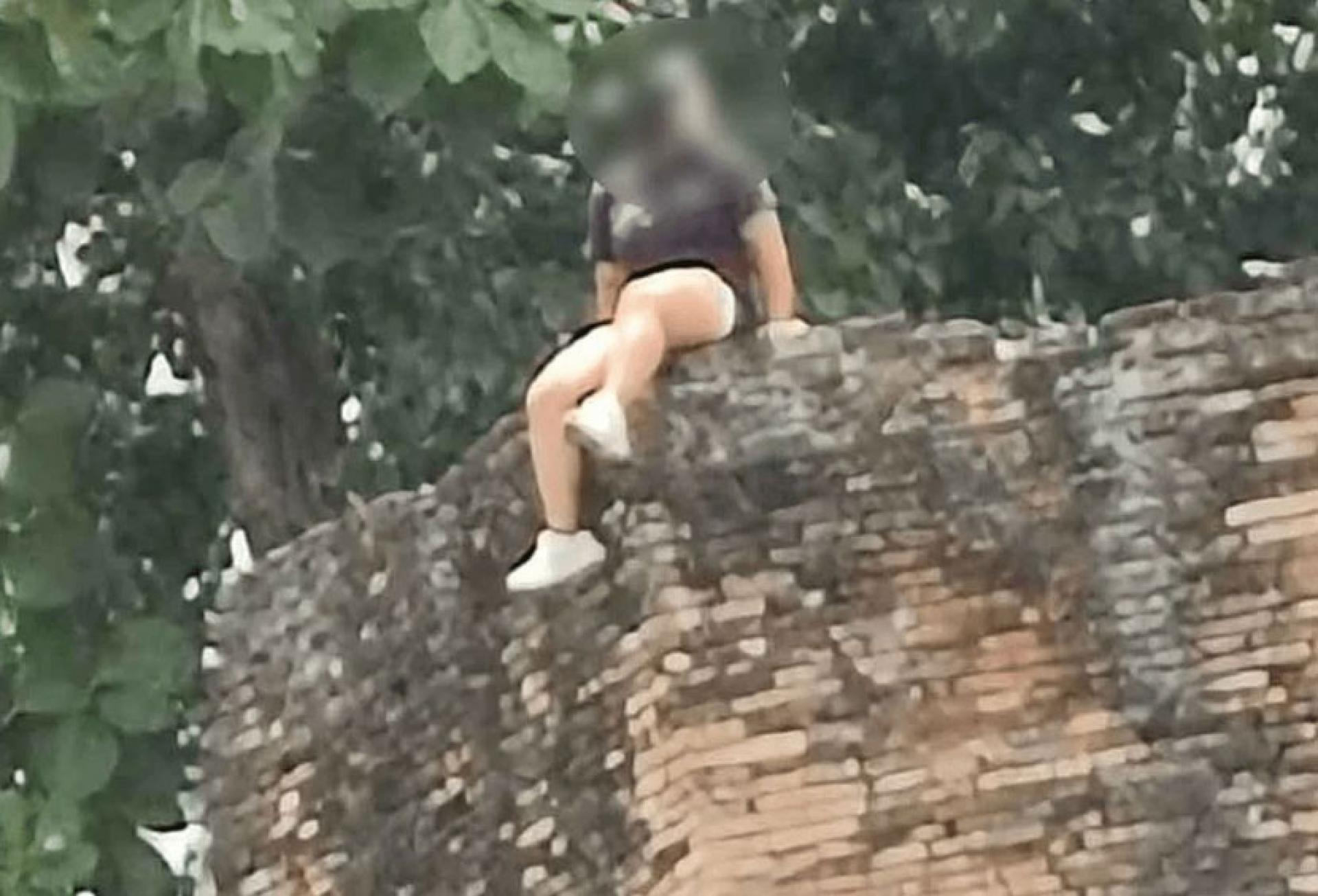涉事女游客坐在古城墙遗迹上拍照。