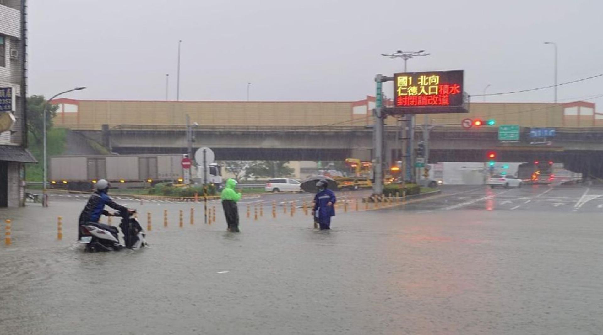 国道1号台南仁德交流道周边23日清晨因雨势出现积淹水，仁德交流道北向入口一度封闭，有机车骑士牵车勉强涉水通过积水路段。