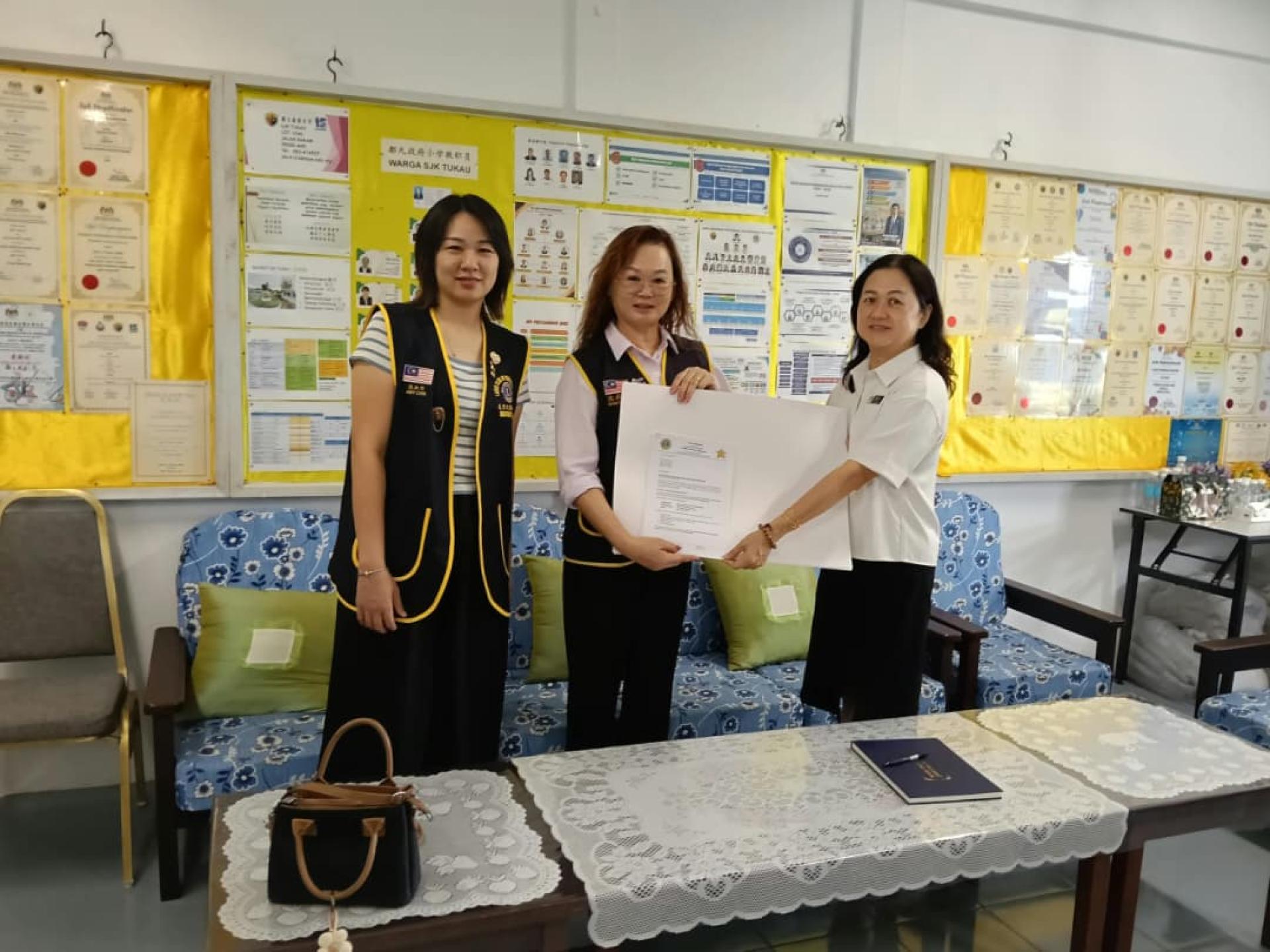 美里文华狮子会第一副会长兼筹备会主席池秋燕（中）移交画纸、邀请函及参赛表格予都九政府小学校长林淑鈖。