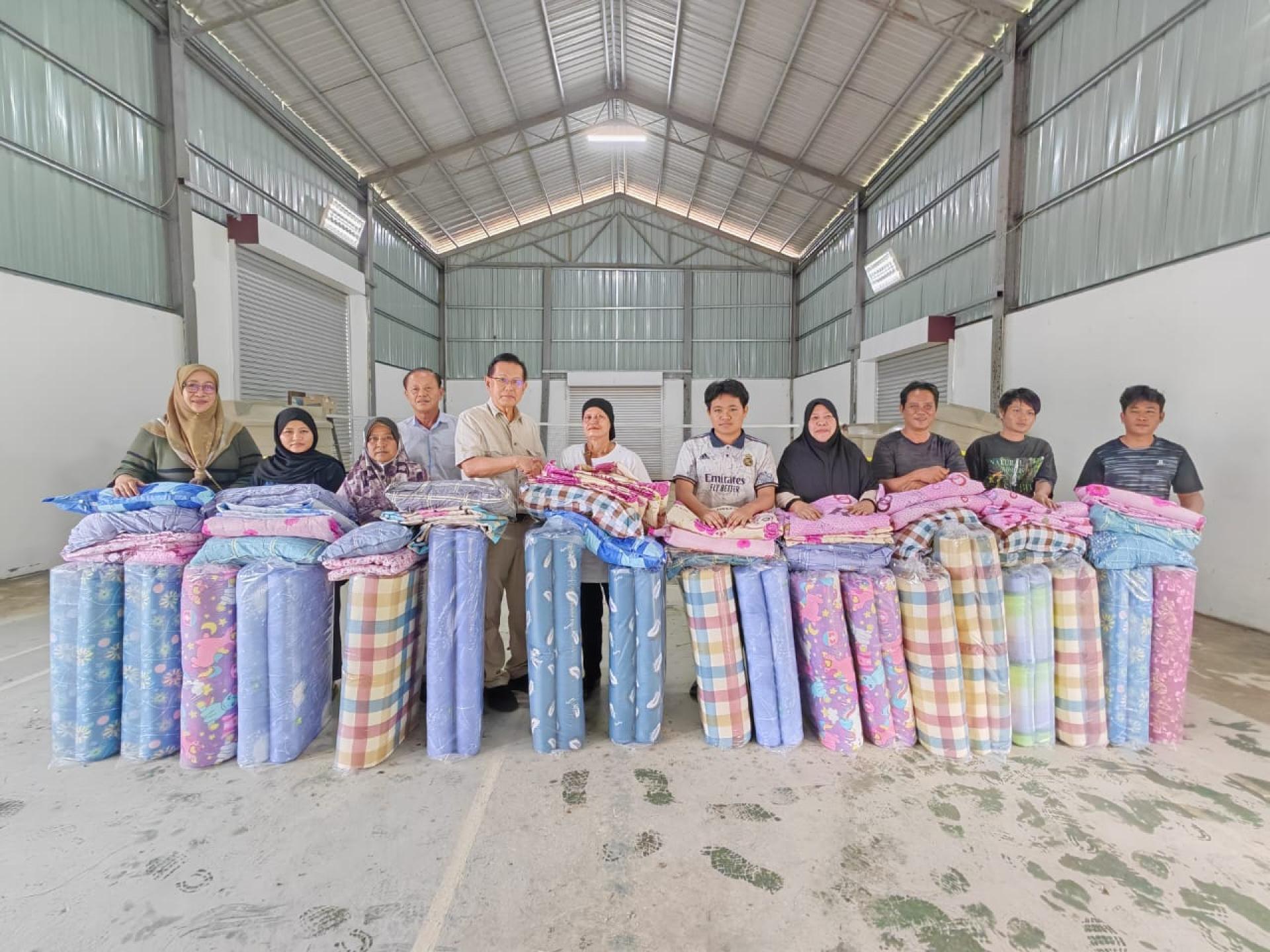 拿督斯里李景胜（左5）移交床褥，被单及枕头给甘榜罗冰加东的9个受灾家庭时摄。左4为甲必丹严学忠。